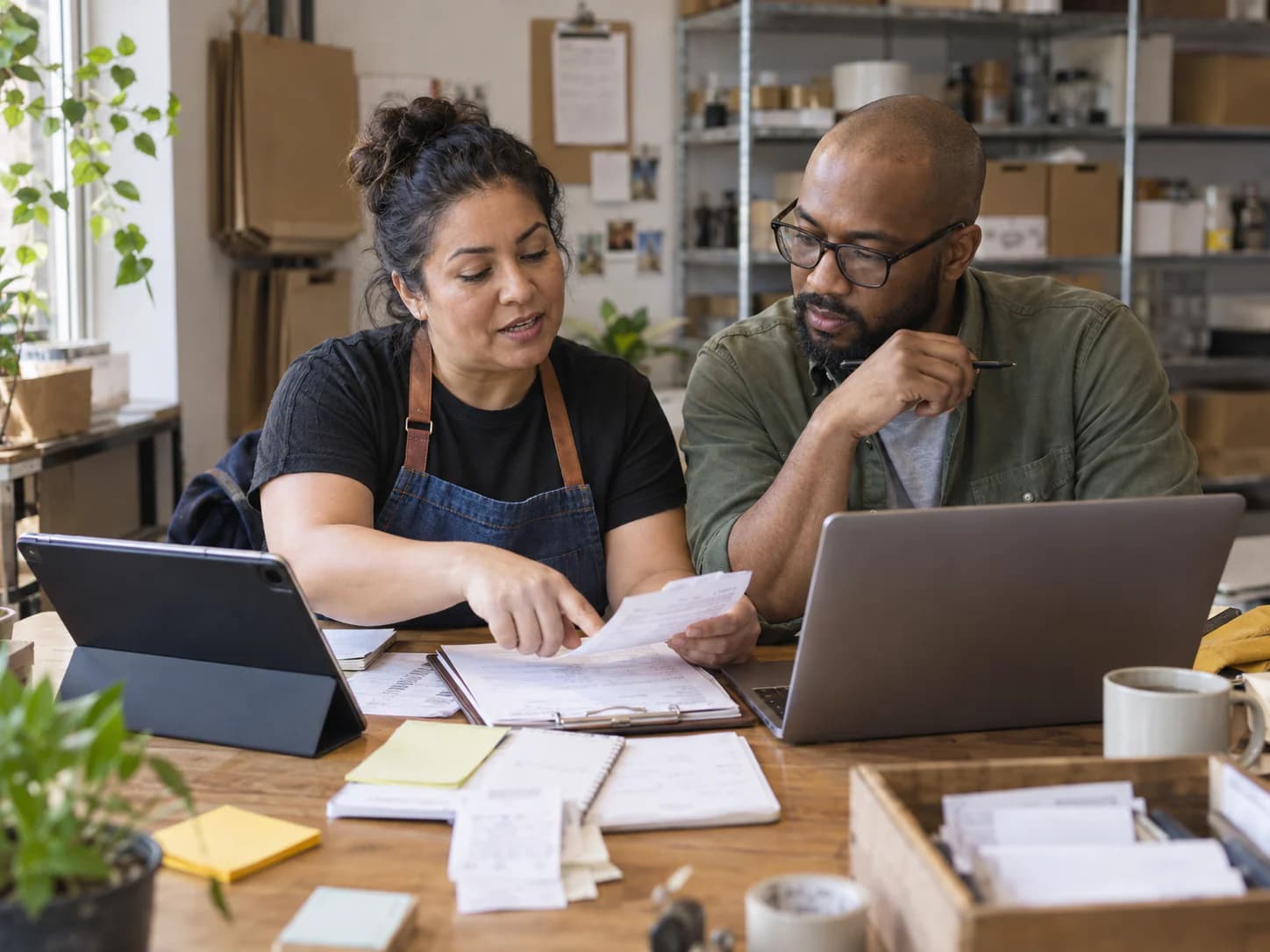 A business operator and advisor reviewing orders, notes, and a workflow together with a tablet and laptop